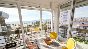 A balcony with a table, chairs, and a view of the beach and buildings.