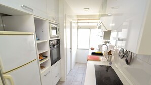 A modern kitchen with white cabinets, a built-in oven, a microwave, and a black induction cooktop.