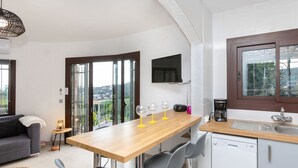 A modern kitchen with a wooden table, two bar stools, a built-in dishwasher, and a window with a view of the countryside. - Wonderful private villa for 6 people with private pool, WIFI, A/C, TV and terrace (Calonge)