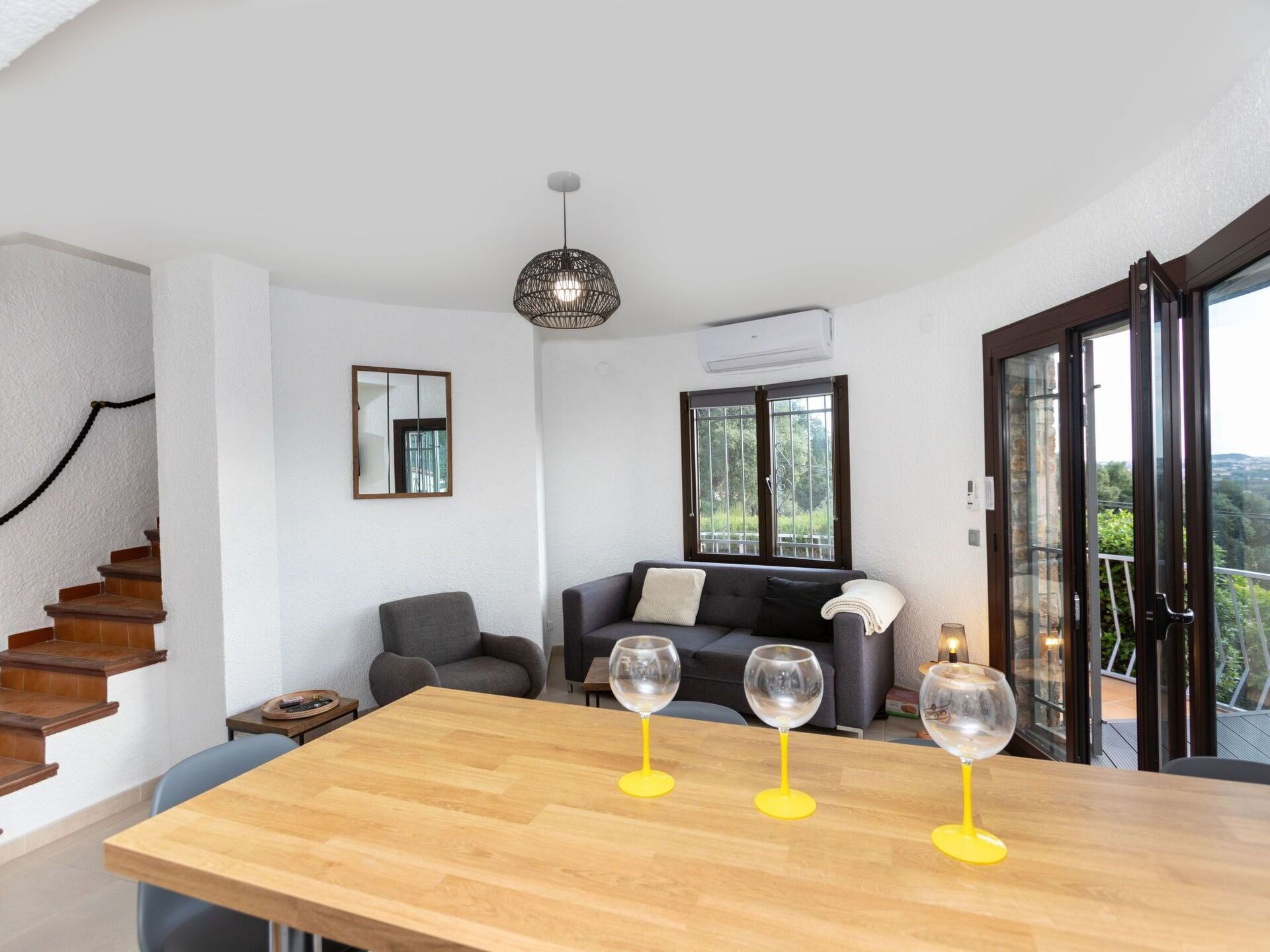 A modern living room with a wooden dining table, a sofa, and a staircase.