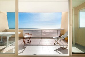 Ein Balkon mit Blick auf den Strand, inklusive Tisch, zwei Stühlen und einem Blumentopf.