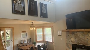A dining area with a wooden table and chairs, a kitchen with a coffee maker, and a stone fireplace. -  Spacious mountain home in Helen Georgia! Innsbruck community HOT TUB! FIRE PIT! (Helen)