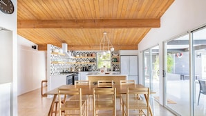 Eine moderne Küche mit Holzbalkendecke, einem Essbereich mit großem Tisch und Stühlen sowie durch Glastüren erreichbarem Außenbereich.