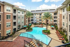 A multi-story residential building with a central courtyard featuring a swimming pool, outdoor seating, and palm trees. - Cool haven in the city, close to the medical center and NRG. (Houston)