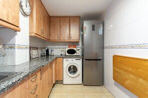 A compact kitchen with wooden cabinets, a washing machine, a microwave, and a refrigerator. - Coral Apartment: Exclusivity and Comfort in the Heart of Tossa de Mar (Tossa de Mar)
