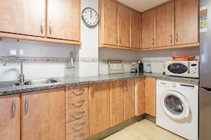 A kitchen with wooden cabinets, a washing machine, a microwave, and a clock.