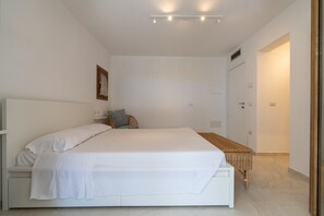 A bedroom with a large bed, a bedside table, a small chair, a bedside lamp, and a door. - Villa "The Beach" with Sea View, Shared Terrace & Wi-Fi (Pittulongu)