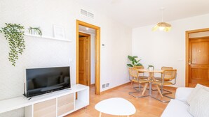 Una sala de estar moderna con un televisor de pantalla plana, un sofá blanco, una mesa de comedor con sillas y un ventilador de techo.