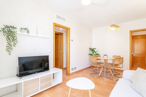 Un salon moderne doté d’un téléviseur à écran plat, d’un canapé blanc, d’une table à manger avec des chaises et d’un ventilateur de plafond.