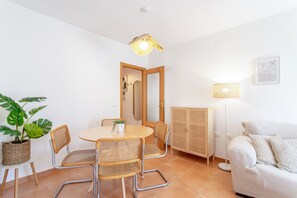 Une pièce comprenant une table ronde en bois, quatre chaises en osier, un canapé blanc, un lampadaire, un meuble et une plante en pot.