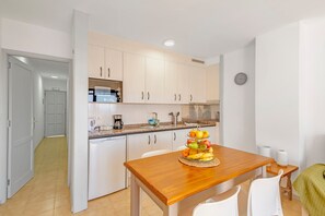 Una cucina compatta con mobili bianchi, un tavolo da pranzo in legno con un centrotavola di frutta e un piccolo tavolino.