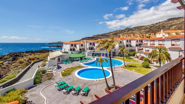 Ett semesterhotell med en swimmingpool, solstolar och utsikt över havet.