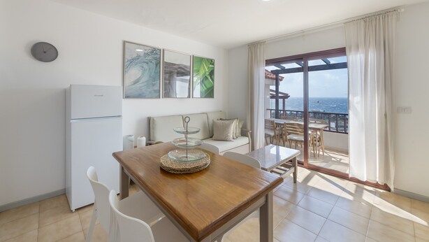 Una cocina moderna con una mesa de comedor, sillas blancas, un refrigerador y un balcón con vistas.