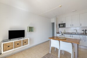 Et moderne køkken med hvide skabe, en mikrobølgeovn og et spiseområde med et træbord og hvide stole.