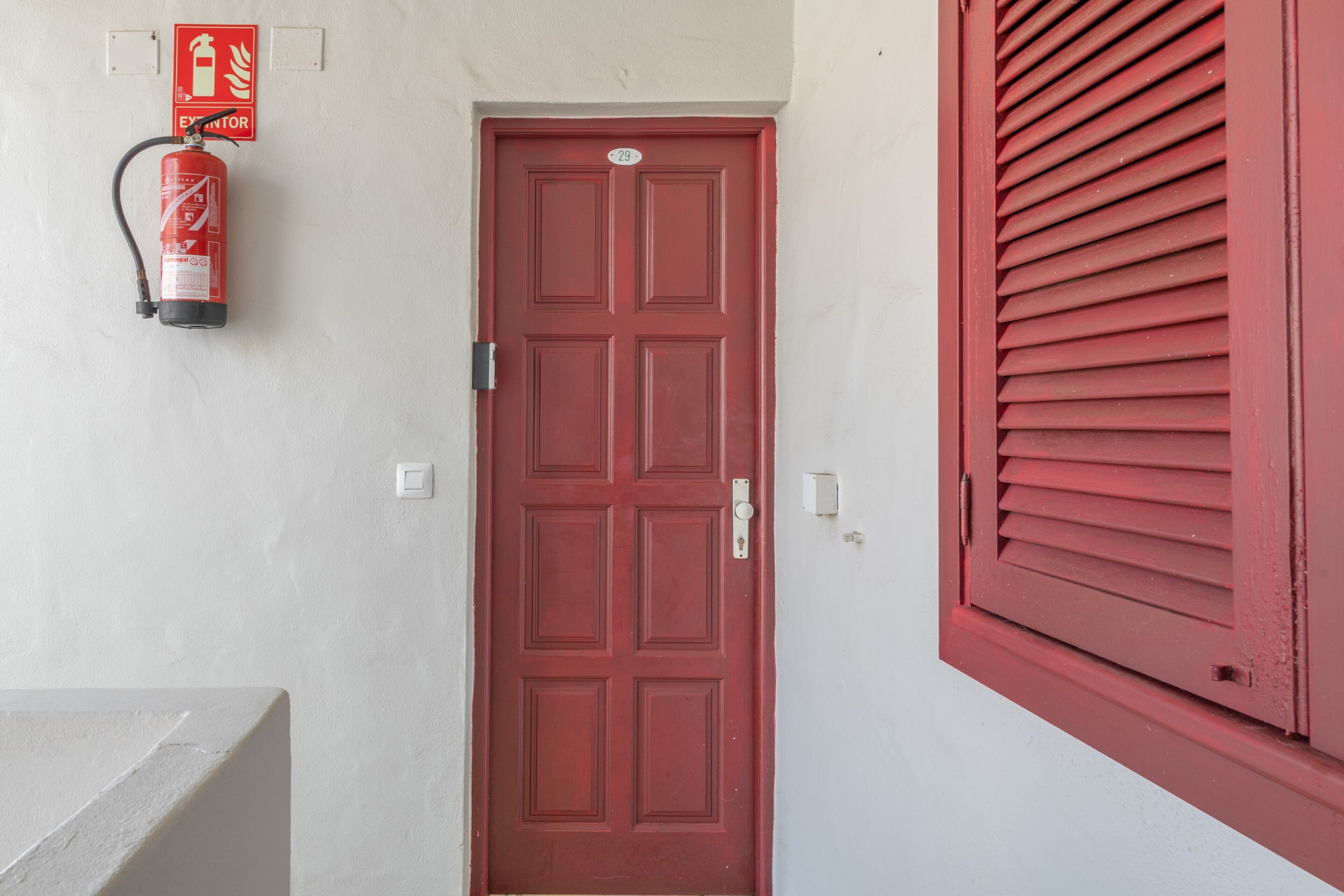 A red door with a fire extinguisher mounted on the wall above it.