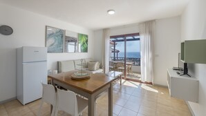 Una cocina moderna con refrigerador, una mesa de comedor con sillas, un televisor y un balcón con vistas.