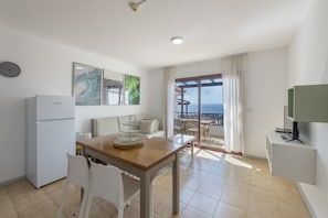 A modern kitchen with a refrigerator, a dining table with chairs, a TV, and a balcony with a view.
