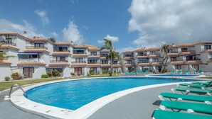Una piscina con sillones de descanso, cielo despejado y un edificio con balcones.