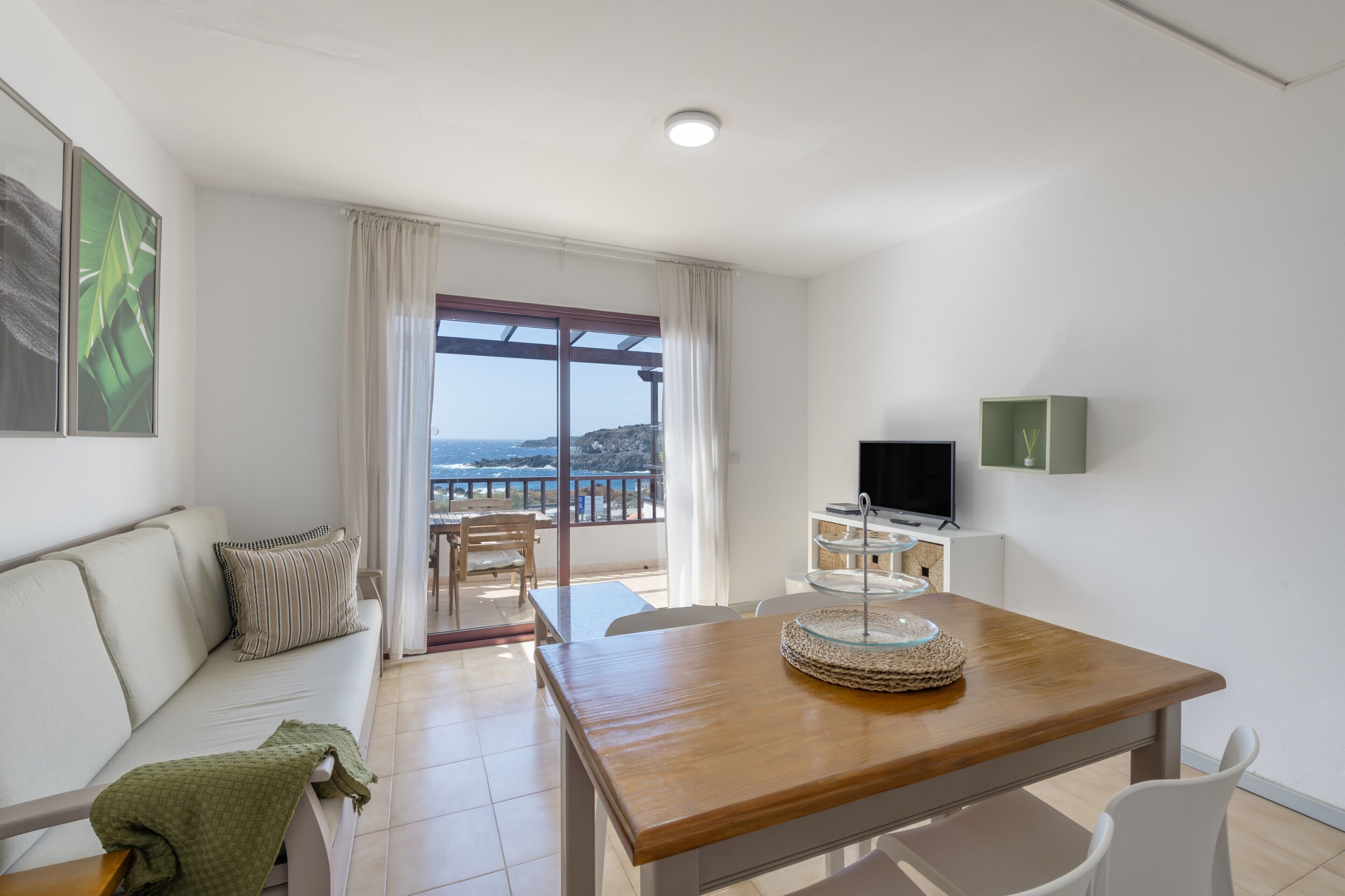 Ein modernes Wohnzimmer mit einem Holzesstisch, einer Couch, einem Fernseher und einem Balkon mit Blick.