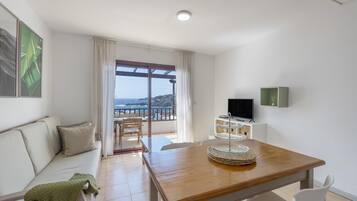 Ein modernes Wohnzimmer mit einem Holzesstisch, einer Couch, einem Fernseher und einem Balkon mit Blick.