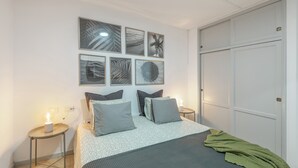 Un dormitorio con cama, mesitas de noche, armario y cuadros en la pared.