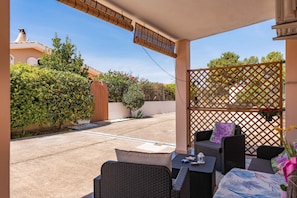 A covered outdoor seating area with wicker furniture, a lattice screen, and a view of the street and greenery.