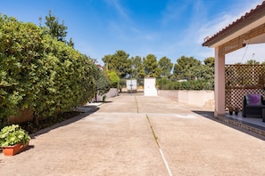 A paved patio area with a pergola, potted plants, and a view of a building in the distance.