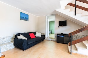 A living room with a sofa, a TV, a staircase, and a door leading to another room.