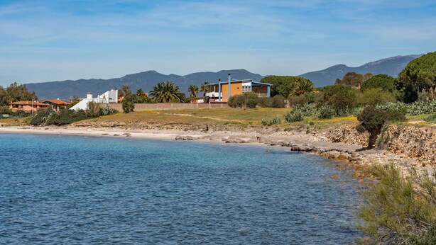 Ein Küstenanwesen mit Strand, Bergen und blauem Himmel.