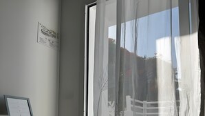 Een kamer met een houten plank, een ingelijst certificaat en een licht doorschijnend gordijn met een bladmotief.