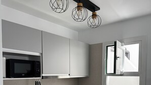 Een moderne keuken met witte kastjes, een zwarte magnetron, een spoelbak en een raam.