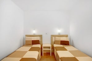 A small, clean room with two single beds, a small table, and two wall-mounted lights.