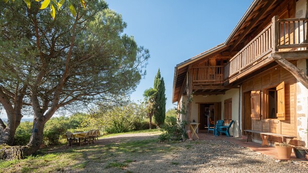 A rustic wooden building with a balcony, a gravel path, and a large tree. - La Toumet – Family Home with Pool and Pyrenees View (MALABAT)