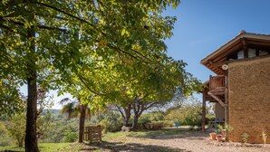 A rustic building with a stone exterior, a wooden deck, and a view of a lush landscape. - La Toumet – Family Home with Pool and Pyrenees View (MALABAT)