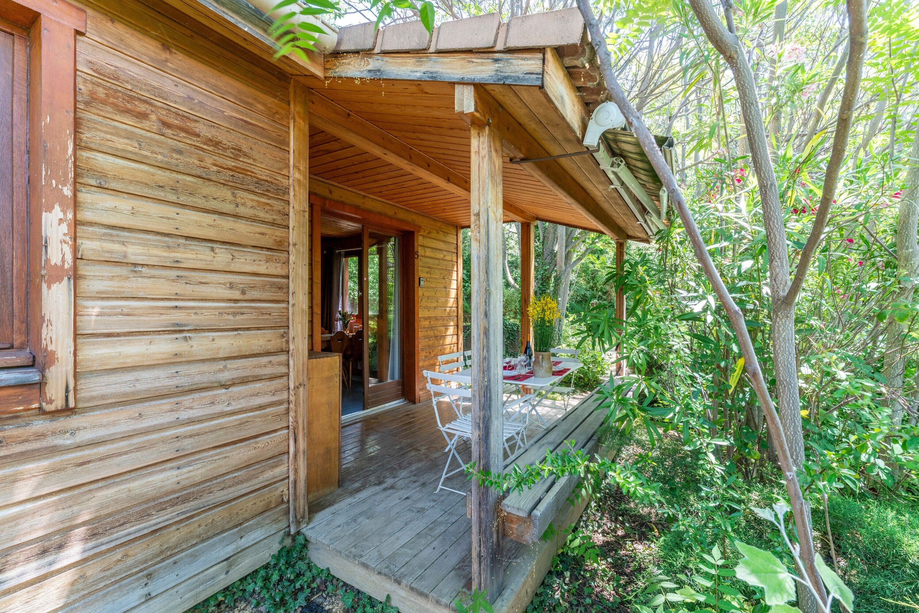 Een houten hut met een veranda, buiten zitplaatsen en een deur naar de binnenruimte.
