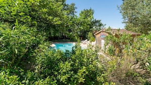 A swimming pool surrounded by lush greenery, a wooden building with a tiled roof, and a clear blue sky. - Chalet 'Gite Thym' with Shared Pool, Private Terrace and Wi-Fi (Mirabel-aux-Baronnies)