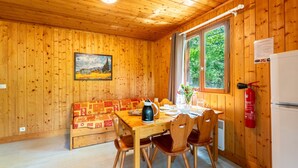 A wooden cabin interior with a dining table, chairs, a sofa, a painting, a window, and a fire extinguisher. - Chalet 'Gite Thym' with Shared Pool, Private Terrace and Wi-Fi (Mirabel-aux-Baronnies)