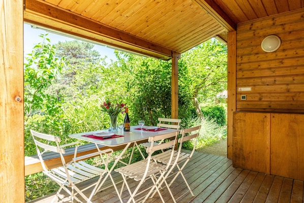 Une terrasse extérieure en bois, avec une table et des chaises, entourée de verdure.