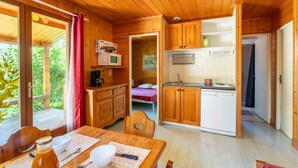 A wooden cabin with a dining area, kitchen, and a bedroom with a view.