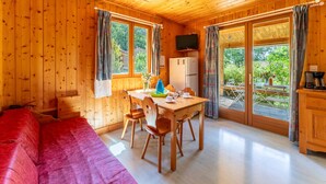 A wooden cabin with a dining table, chairs, a TV, and a sofa. - Chalet 'Gite Sariette' with Shared Pool, Private Terrace and Wi-Fi (Mirabel-aux-Baronnies)