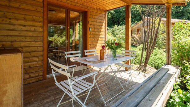 A wooden deck with a table and chairs, a wooden bench, and a glass door leading to an outdoor area. - Chalet 'Gite Sariette' with Shared Pool, Private Terrace and Wi-Fi (Mirabel-aux-Baronnies)