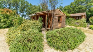A wooden cabin with a porch, surrounded by dense greenery and a gravel path. - Chalet 'Gite Sariette' with Shared Pool, Private Terrace and Wi-Fi (Mirabel-aux-Baronnies)