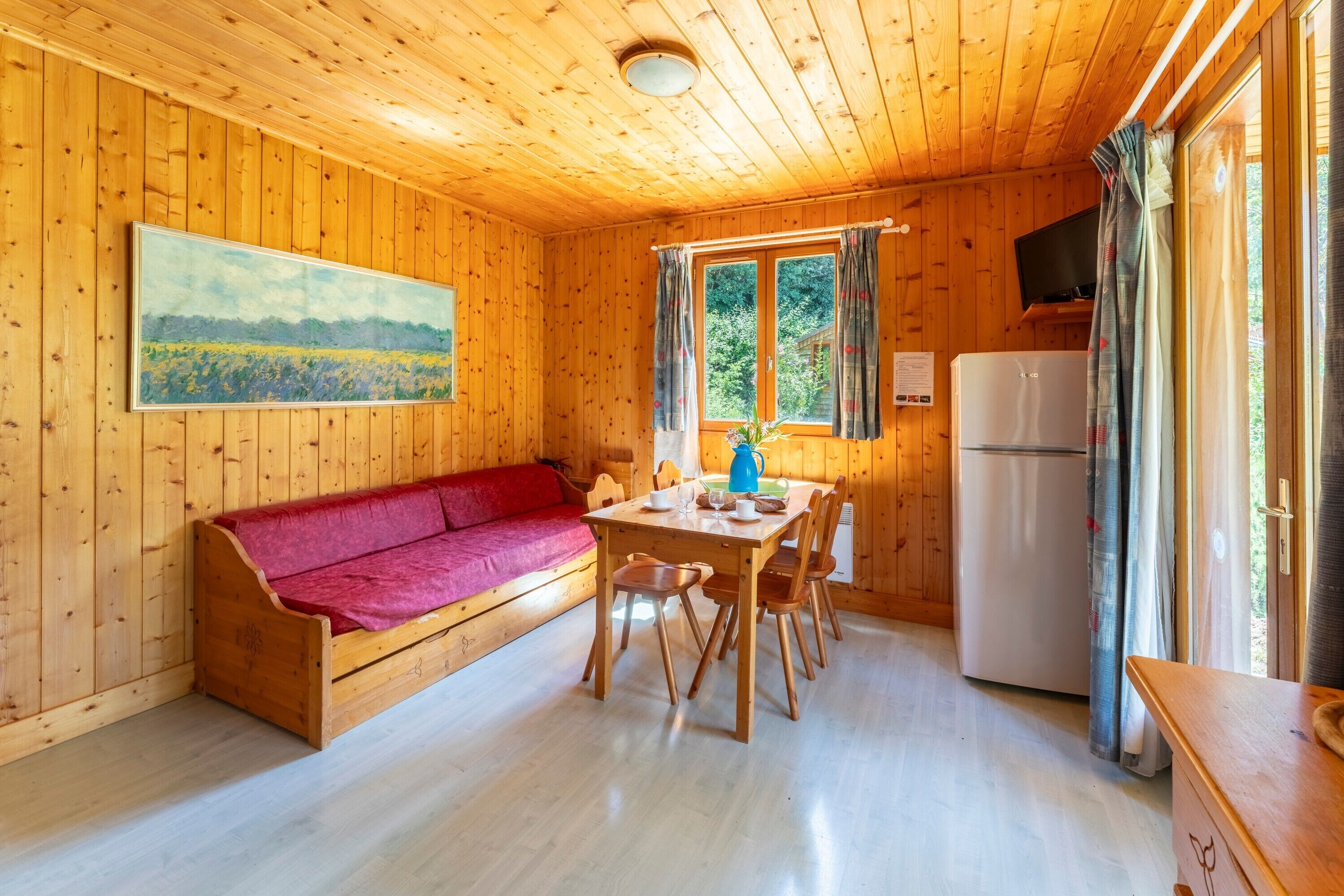 Une cabane en bois avec un canapé, une table à manger, des chaises, un réfrigérateur et un tableau accroché au mur.