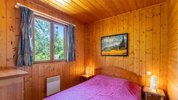 Une pièce de style cabane en bois, avec un lit, une fenêtre avec des rideaux, un tableau au mur et un radiateur.