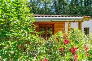Ein hölzernes Haus mit Ziegeldach, umgeben von üppigem Grün und blühenden Pflanzen.