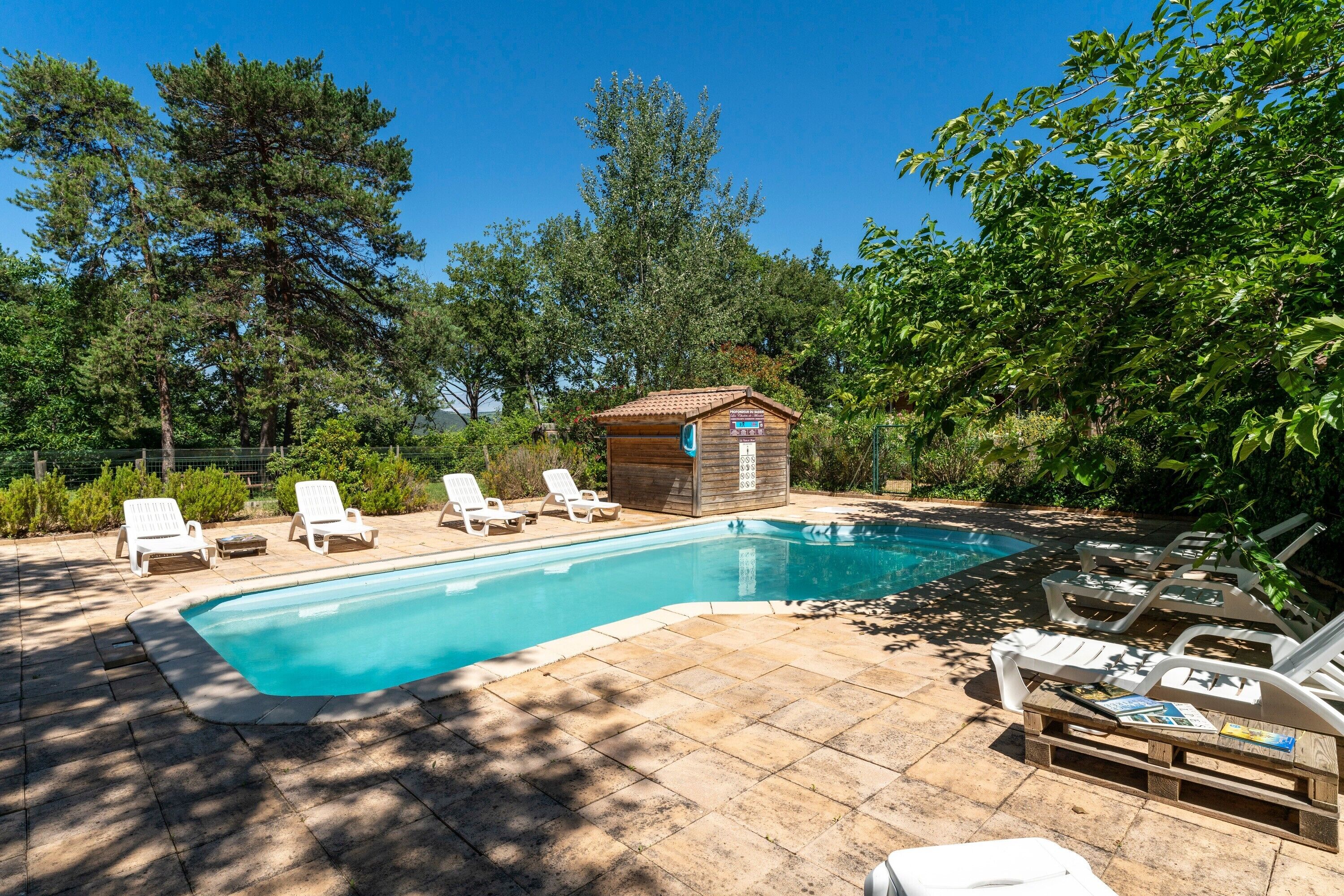 Una piscina rectangular con cubierta de madera, rodeada de sillones blancos y una pequeña cabaña de madera.
