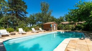 Una piscina rectangular con agua azul cristalina, rodeada de sillas de descanso y una cabaña de madera.