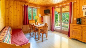 A wooden cabin with a dining table, chairs, a sofa, a television, a refrigerator, and a coffee maker. - Chalet 'Gite Lavande' with Shared Pool, Private Terrace and Wi-Fi (Mirabel-aux-Baronnies)
