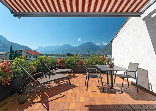 A terrace with a view of mountains, a table with chairs, and a small garden area.