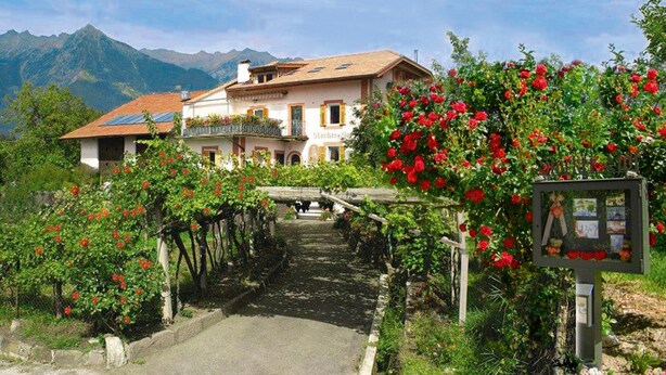A building with a garden, a stone pathway, and mountains in the background. - Apartment 'Stöckerhof  Traube' with Mountain View, Shared Pool and Wi-Fi (Merano)